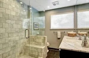 A bathroom featuring a large glass-enclosed walk-in shower with light square tiles and a marble vanity