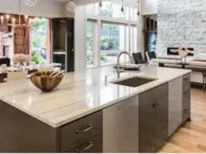 A modern kitchen island with a light marble countertop, a sink, and dark lower cabinets