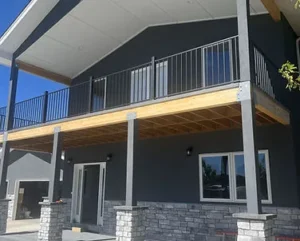 A two-story modern dark gray house with a prominent upper wooden deck and black metal railings