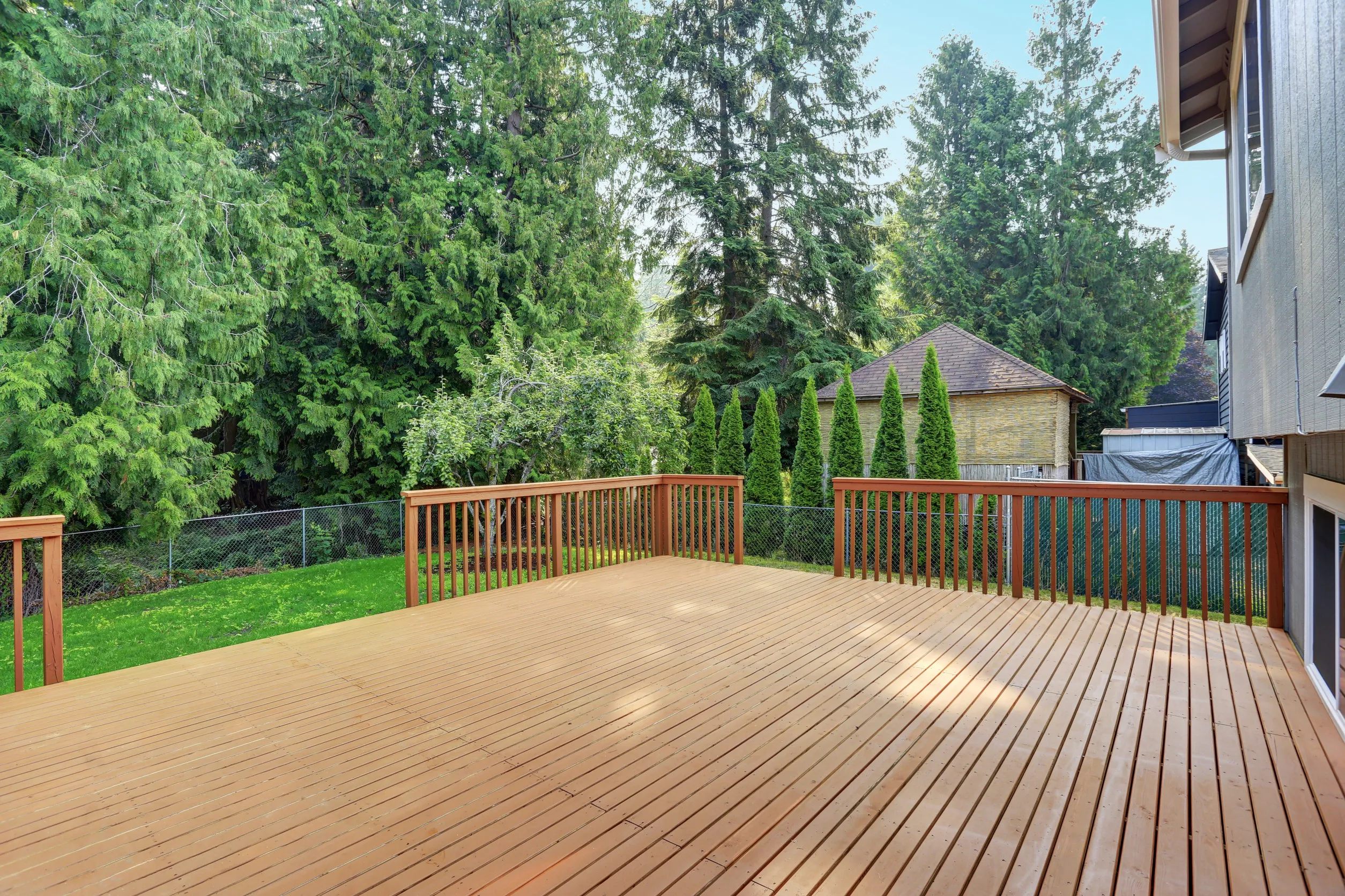 Empty walkout deck boasts redwood railings overlooking well kept back yard